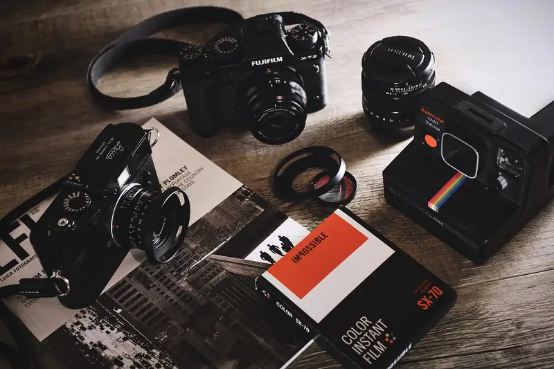 Vintage film cameras, lenses, a Polaroid camera and film boxes spread across a wooden table