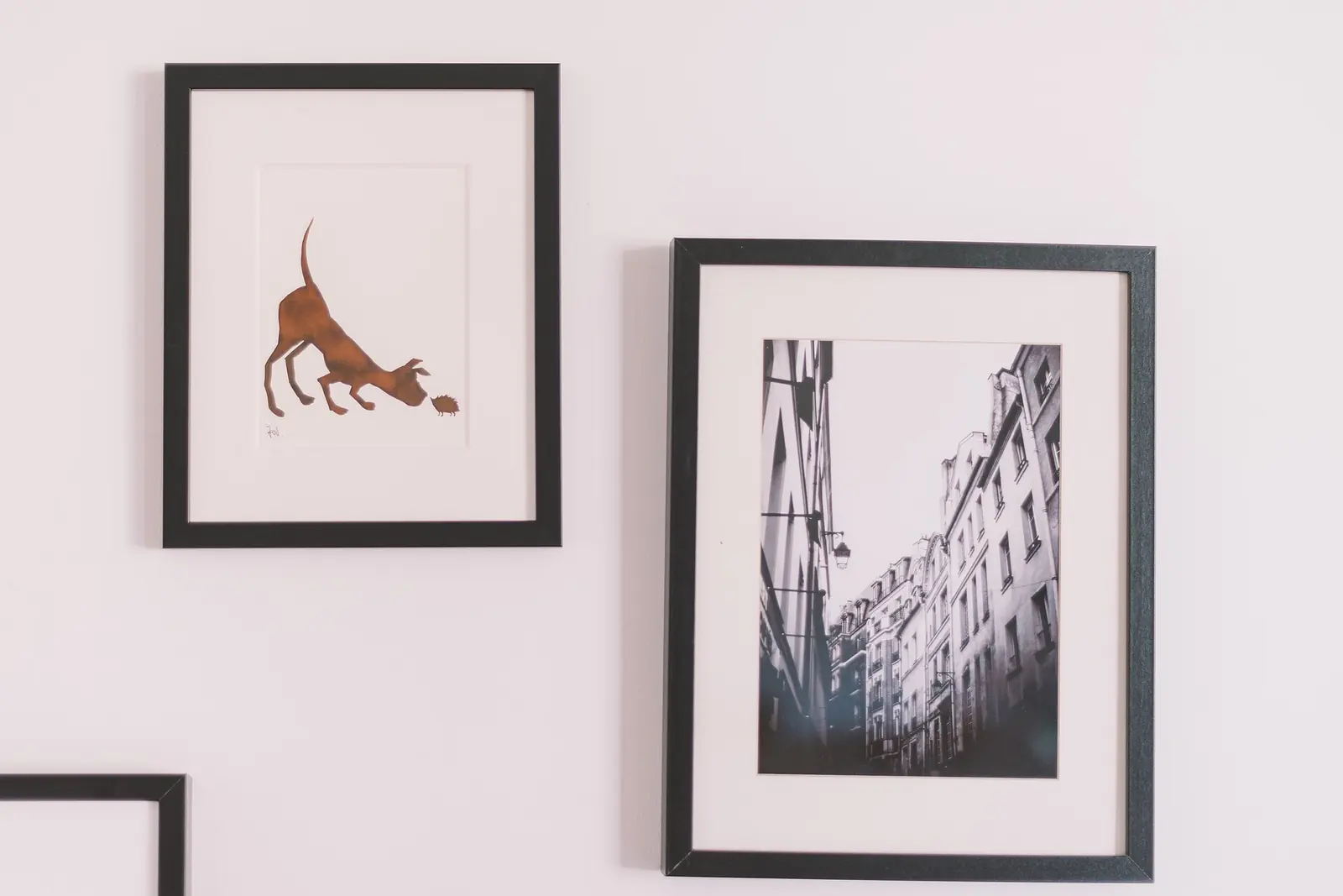 Black-framed prints, including a sketch of a cat and a black-and-white street photo, hang on a pale pink wall