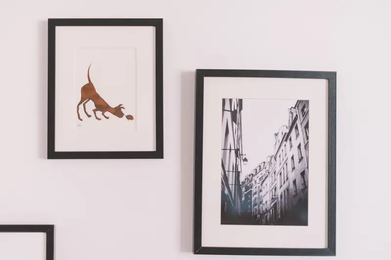 Black-framed prints, including a sketch of a cat and a black-and-white street photo, hang on a pale pink wall