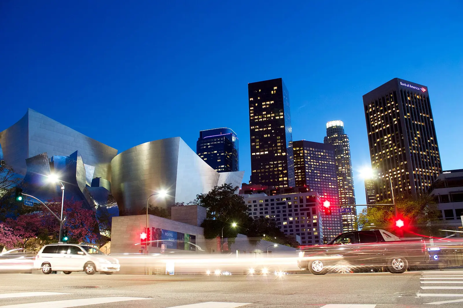 Downtown Los Angeles skyscrapers and the curved steel of Walt Disney Concert Hall at dusk, with light trails on the street