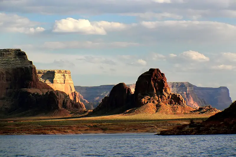 Red rock buttes and mesas rise from the blue water of Lake Powell under puffy white clouds