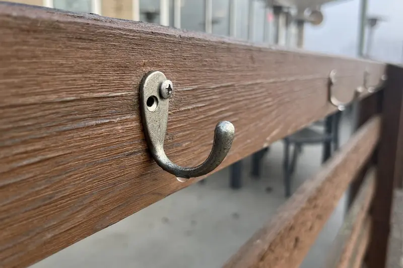 A row of metal coat hooks mounted along a wooden rail, with a foggy patio blurred behind