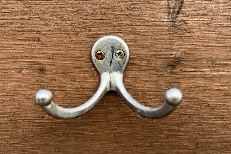 Close-up of a silver double coat hook screwed into a wooden board